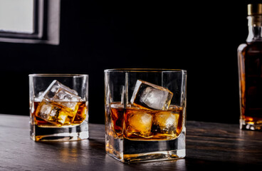 Glass of whisky with ice on dark wooden table and black background. glass of sophisticated whiskey, ice cubes