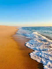 Deurstickers Warm colors of the seascape, sand sea coastline, sea waves on the sand, clear blue sky, no people, empty beach © Oksana