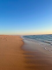 Warm colors of the seascape, sand sea coastline, sea waves on the sand, clear blue sky, no people, empty beach