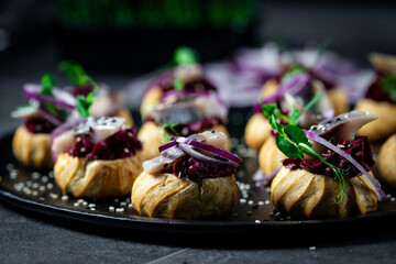 Profiteroles with herring, cottage cheese and red onion on a dark background - obrazy, fototapety, plakaty