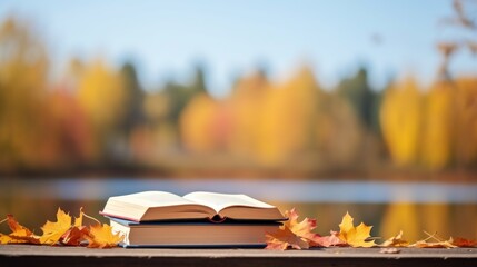 Naklejka na ściany i meble Books on autumn orange, yellow, purple leaves and blurry landscape and cloudy blue sky in background with copy space