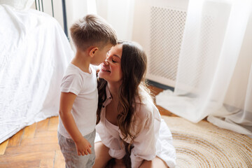 Toddler boy in pajama kissing nose of smiling mother in bedroom in morning