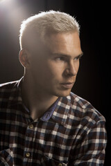 Portrait of an attractive man with blond hair in a checkered shirt on a black background.