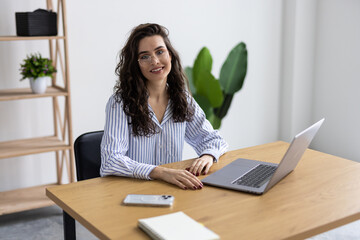 Happy and smiling businesswoman typing on laptop at work inside office building
