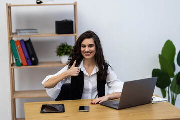 Pretty businesswoman at computer showing thumb up at desk at office