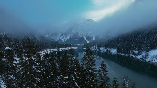 Lake Plansee in Austria in winter with snow. Alps mountains reflection in the dark blue water surface. Beautiful scenic aerial drone.