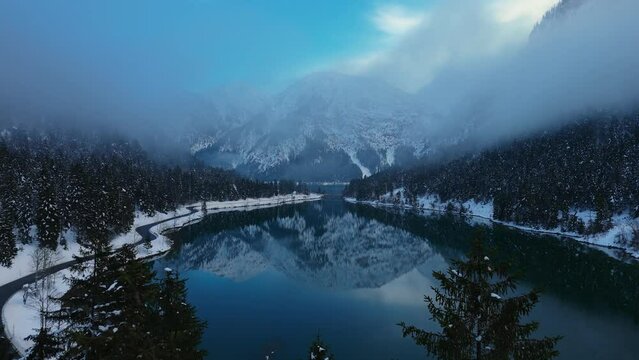 Plansee Lake in Austria in winter. Reflection of alps mountains with snow in the dark blue water surface. Beautiful scenic aerial drone.