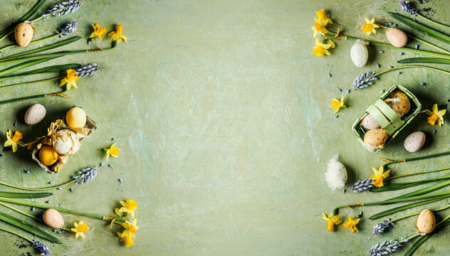 Green Easter background with springtime flowers and Easter eggs, top view. Frame