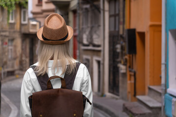 Photo from the back of a young blonde woman in a hat with a backpack on a beautiful historical...