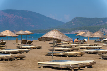 Sun loungers and umbrellas on Iztuzu beach on a sunny day against the background of mountains,...
