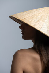 Beauty, fashion, make-up, style concept. Beautiful woman with traditional Asian cane hat studio portrait. Model profile view with naked shoulder and hiding eyes under hat