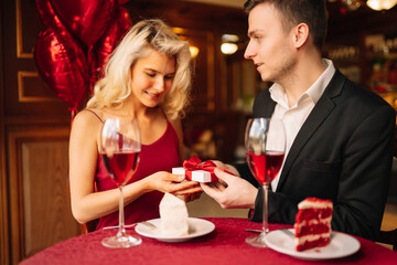 Beautiful young couple celebrating Valentine's Day in the restaurant. Exchange of gifts. Romantic day together.