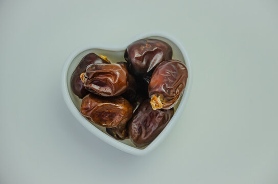 Dried dates in a white plate in the shape of a heart on a white background