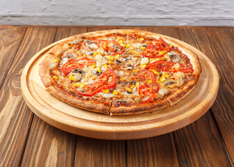 delicious pizza with chicken, mushrooms, cheese, tomatoes and corn on a wooden background