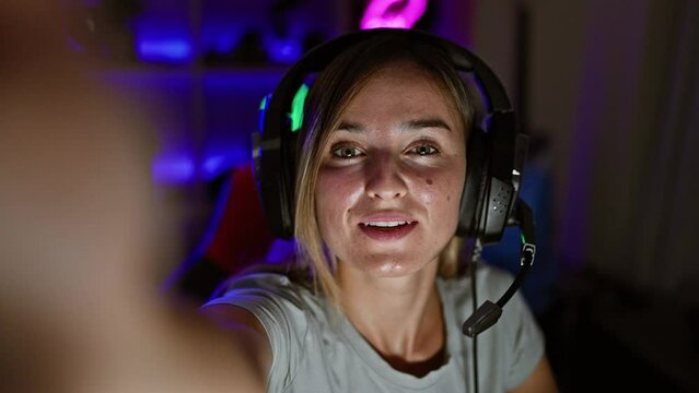 Enthralling stream, blonde beauty streamer smiling on video call, engaging in gaming night, cuddled in dark gaming room at home
