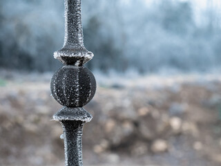 Detail shot of the bars of a security fence in a town frozen by the cercelilla caused by the fog and a stone barrier with a completely frozen and foggy forest around
