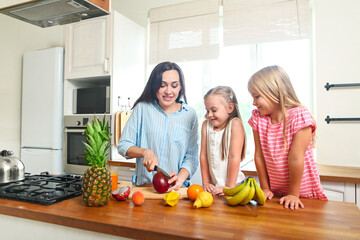 Beautiful little girls with they mother in the kitchen preparing a fruit salad