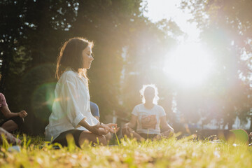 A girl meditates in a park, a yoga instructor conducts a lesson for a group of students, practicing...