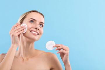 Smiling woman removing makeup with cotton pads on light blue background. Space for text