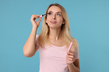 Beautiful woman applying mascara on light blue background