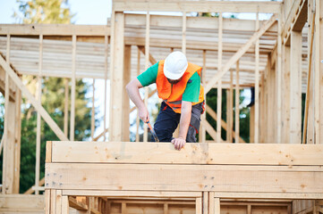 Carpenter constructing two-story wooden frame house. Bearded man hammering nails into structure...
