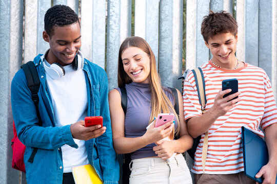  Multiracial Group Of Smiling Students Browsing Smartphone App Outdoors.