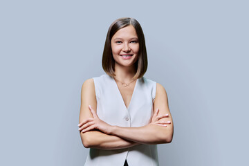 Young confident woman with crossed arms looking at camera on gray background