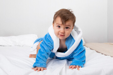 Baby in blue bathrobe, after bath, sitting on bed. Emotions, copy space.