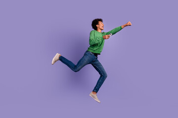 Fototapeta na wymiar Full length photo of excited cool guy wear green pullover running sale modern gadget empty space isolated purple color background