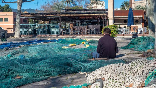 Pescador sentado trabajando en el arreglo de las redes y arneses de pesca. Las redes de pesca están distendidas al sol para secarse. Fotografía tomada en la Lonja del pescado de Palma de Mallorca
