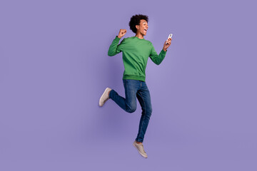 Fototapeta na wymiar Full length photo of excited lucky man dressed green sweater jumping winning game device empty space isolated violet color background