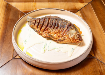 Whole fried fish on a plate. On a wooden table.