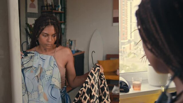 Over shoulder footage of gen Z Black woman choosing outfit looking at mirror at home while getting ready for walkOver shoulder footage of gen Z Black woman choosing outfit looking at mirror at home wh
