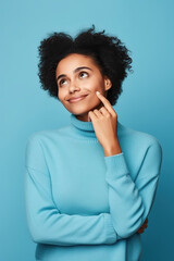 Fototapeta na wymiar Cute African American lady thinking about her inspiration touch chin looking mockup choosing product option isolated on blue color background