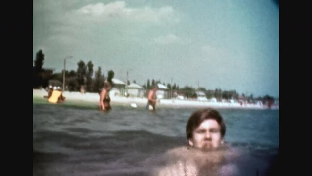 People swim in sea water in summer beach resort. Woman, young man swimming in ocean on sunny vacation. Happy holiday. Fun activity in water. Home movies. Lifestyle archive. Vintage color film 1980s