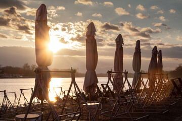 Selective blur on cafe tables and sun umbrellas closed on the beach of savsko jezero lake in Ada...