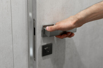 A persons hand is captured as it grasps a sleek, contemporary handle, preparing to open a light grey door.