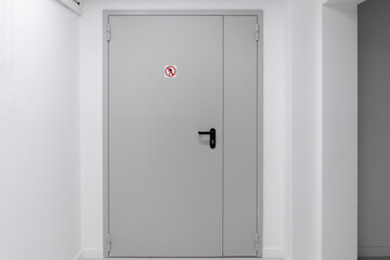 This image shows a closed white door in a contemporary building with a clear no entry sign affixed...