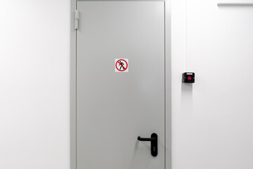This image shows a closed white door in a contemporary building with a clear no entry sign affixed...