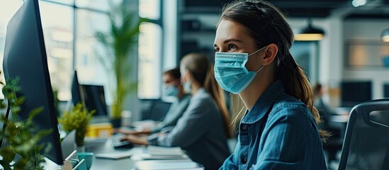 Young businesswoman and her colleague wearing face masks while working on a computer in the office during virus epidemic. Copy space image. Place for adding text