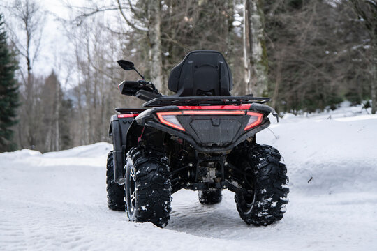 A red and black quad bike stands idle on a snow-covered trail, its presence contrasting with the serene, white winter landscape.