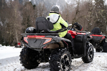 A man, equipped with cold-weather attire, confidently handles a red quad bike along a snowy path,...