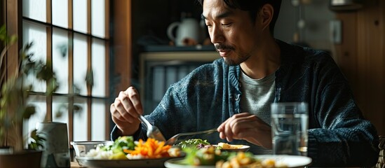 Asian attractive handsome male eating green salad in kitchen at home Active young man sit on table...