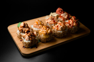 Sushi rolls with sesame and various fillings and sauces lie on a wooden board
