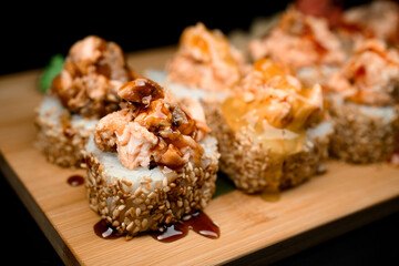 Focus on one sushi roll with sesame, filling and sauce lying on a wooden board