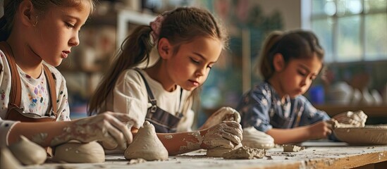 Three children in aprons sitting by table kneading clay and making earthenware at lesson. Copy space image. Place for adding text