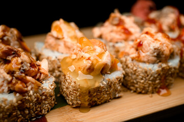 Focus on one sushi roll with sesame, filling and transparent caramel colored sauce lying on a wooden board