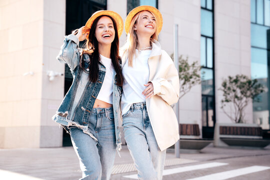 Two young beautiful smiling hipster female in trendy summer clothes. Carefree women posing in the street. Positive models having fun outdoors at sunny day. Cheerful and happy. In hat and sunglasses