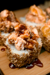 Focus on one sushi roll with sesame, filling and unagi sauce lying on a wooden board