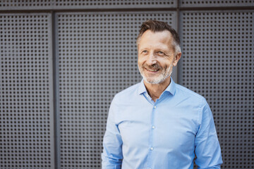 Successful Bestager Businessman in Blue Shirt Laughing, Standing confidently against Metal Wall.